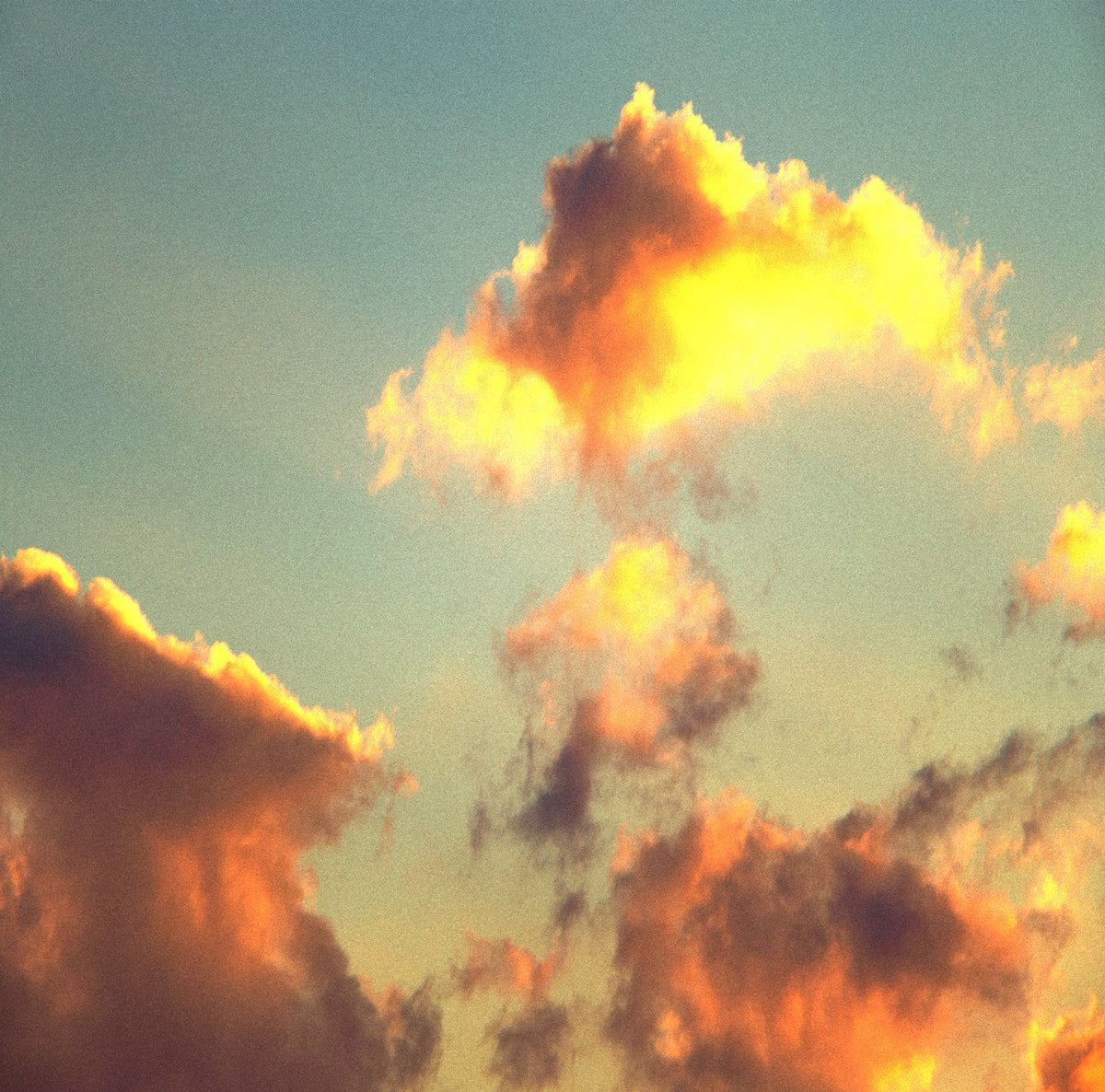 Sunlit clouds with bright yellow and orange highlights against a pale blue sky.