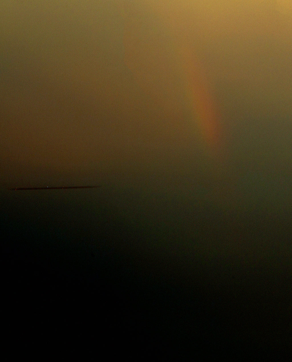 A very dark, low-contrast scene with a faint warm glow near the top and a faint vertical rainbow-like light, plus a thin horizontal streak on the left. 