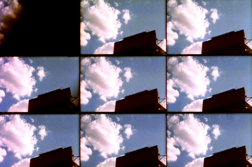 A collage-style grid of repeated sky scenes showing blue sky with large white clouds and the dark silhouette of a building, with one black square in the upper left.